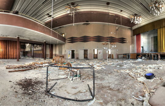 Verlassener Saal mit Bühne und Balkon.